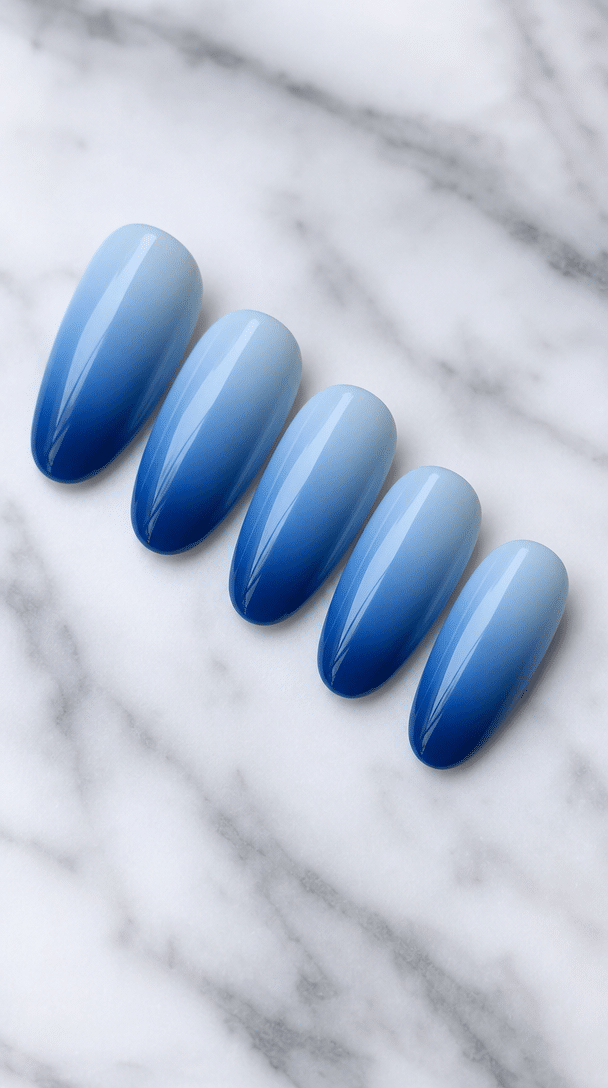 Five gradient blue ombre nails on a marble surface.