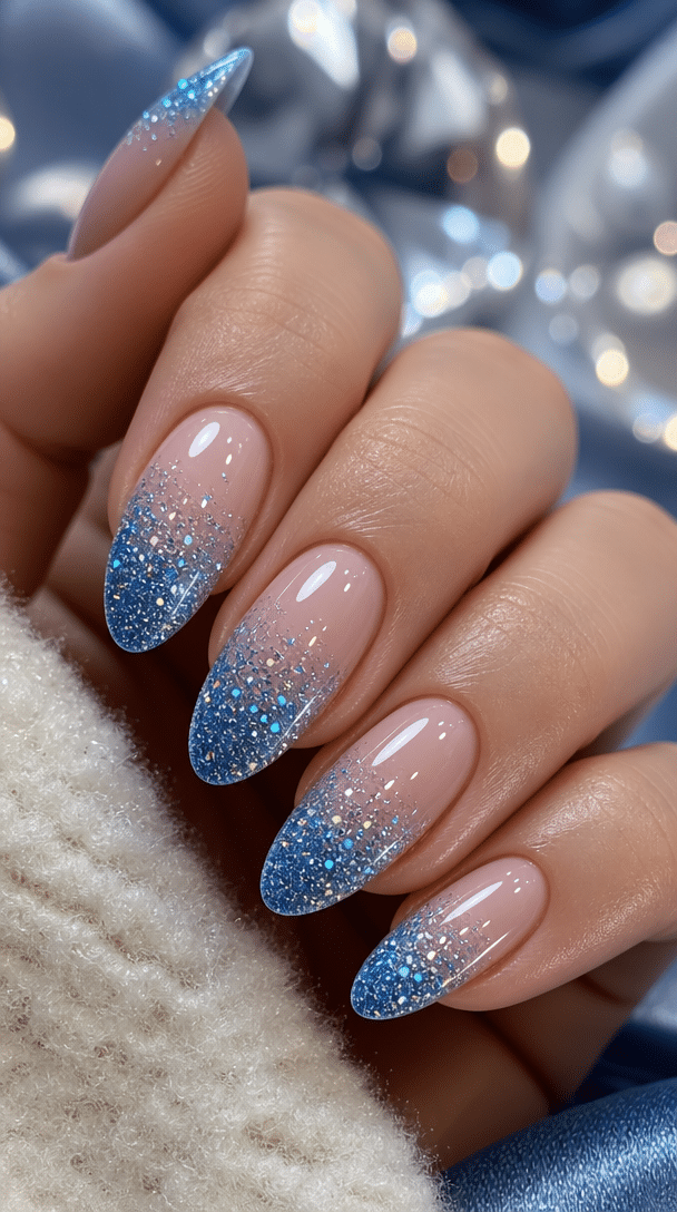 Close-up of nails with sparkling blue glitter accents, showcasing a gradient effect with a light pink base.