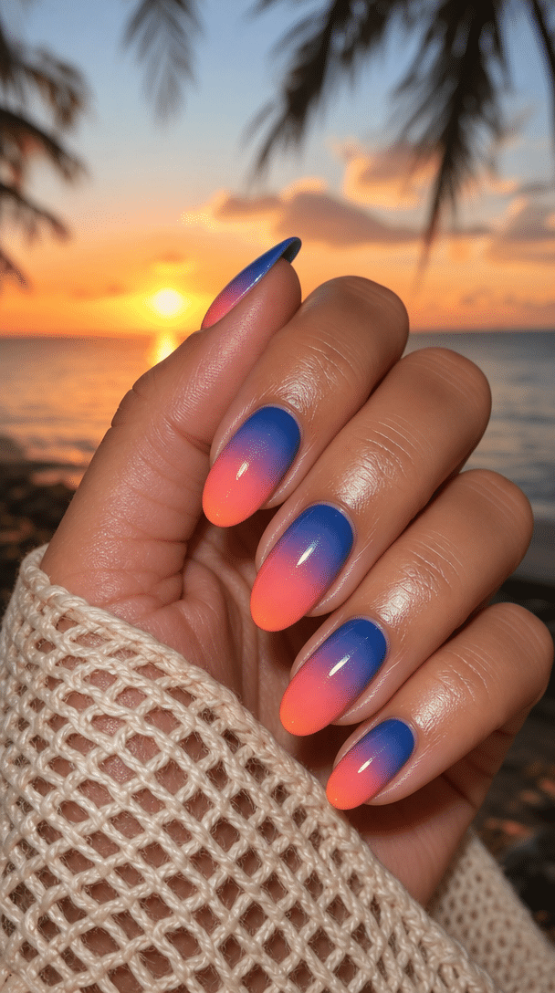 A hand with tropical sunset ombre nails featuring bright blue and coral colors against a sunset backdrop.